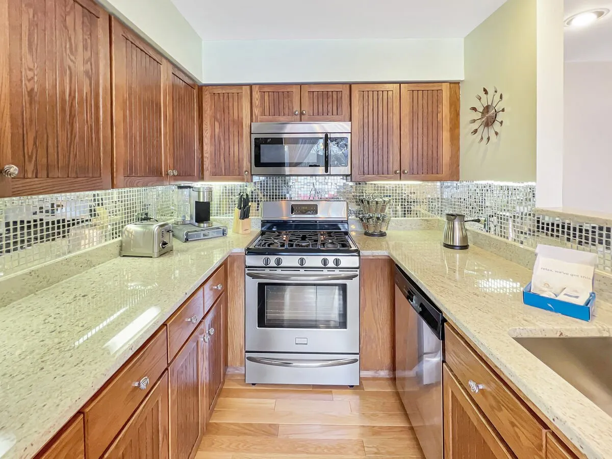 A modern, well-equipped kitchen with stainless steel appliances, granite countertops, wooden cabinets, and a stylish mosaic backsplash. Ample space invites cooking, entertaining, and gathering for shared meals.