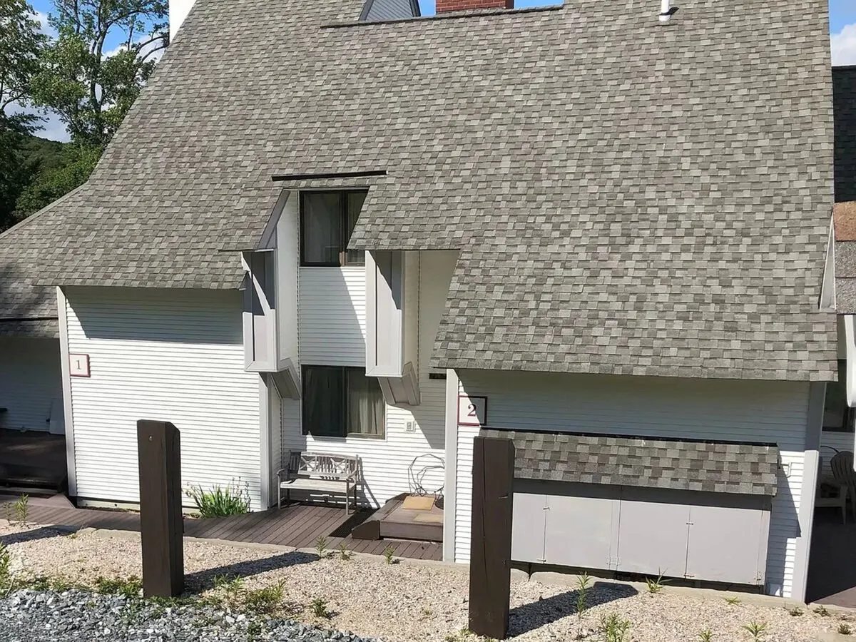 An exterior view of the Sunrise Mountain Village Resort featuring its modern asymmetrical rooflines, front seating areas, and several numbered entryways. Residents are seen relaxing on the porch, enjoying sunset views and the surrounding natural landscape. The atmosphere is welcoming, with hints of nearby community events and easy access to outdoor activities.