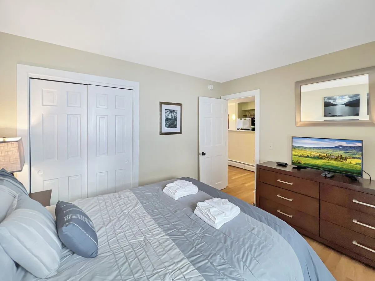 A bedroom with a full bed dressed in crisp linens, a television, a dresser, closet doors, and a mirror. The room exudes coziness and offers a restful retreat.