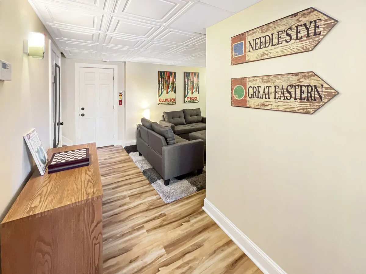 A stylish and inviting community lounge area with a gray sofa, chessboard on a console table, and vibrant wall art. Wooden direction signs add a playful touch, suggesting guidance around the resort. The space feels perfect for après-ski gatherings, socializing, and unwinding after a day on the slopes.