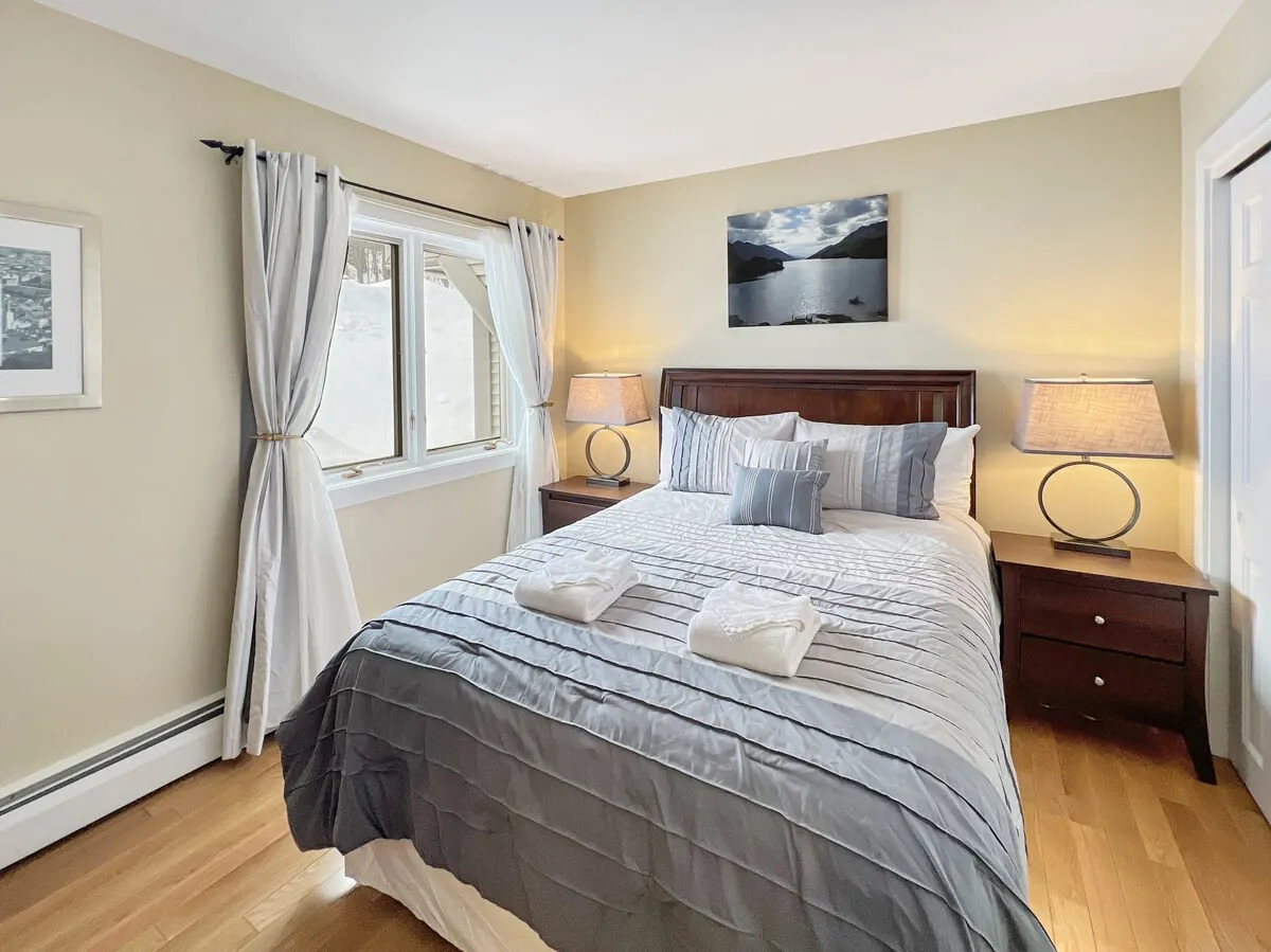 A cozy bedroom with a comfortable bed, matching nightstands, a window that welcomes morning light, and artwork above the bed. The serene, airy feeling of the space evokes a sense of peace ideal for unwinding or greeting the sunrise.