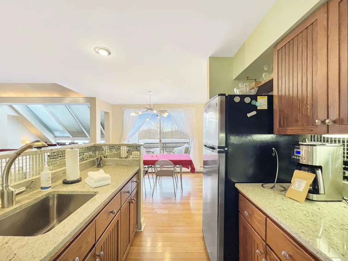This image shows a spacious open-plan kitchen and dining area, featuring a granite countertop, a black refrigerator, a dining table with chairs, and large windows with curtains. The room feels bright and welcoming, ideal for group meals or preparing snacks together after a day on the slopes.