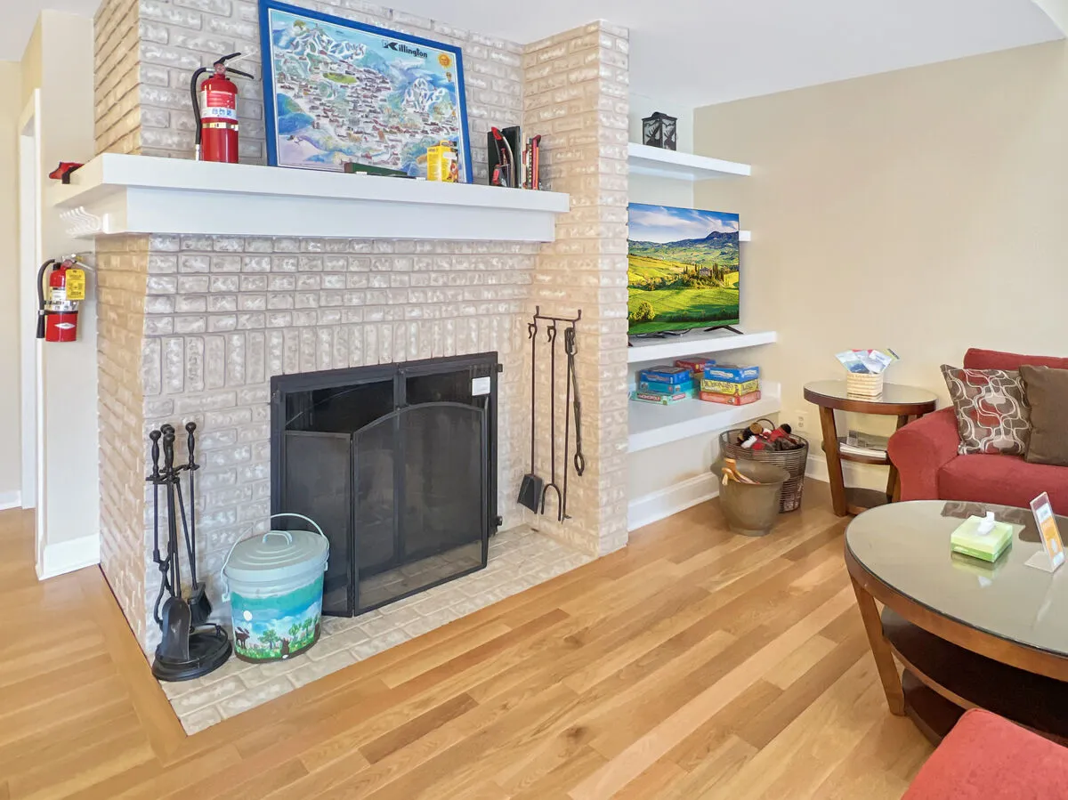 A cozy living area centered around a glowing fireplace, with a bold red couch, shelves filled with decorative items, and a coffee table set for board games. The ambiance is warm and sociable, inviting guests to gather after a day on the slopes.